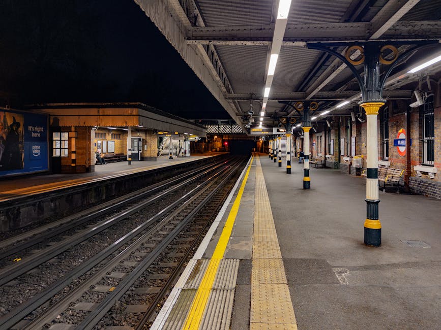 The image depicts a well-maintained platform at Acton Central station, illuminated by overhead lighting, with clean, smooth concrete flooring and tactile paving along the yellow safety line. The platf
